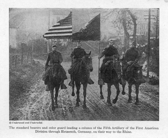 The standard bearers and color guard leading a column of the Fifth Artillery of the First American Division through Hetzerath, Germany, on their way to the Rhine.